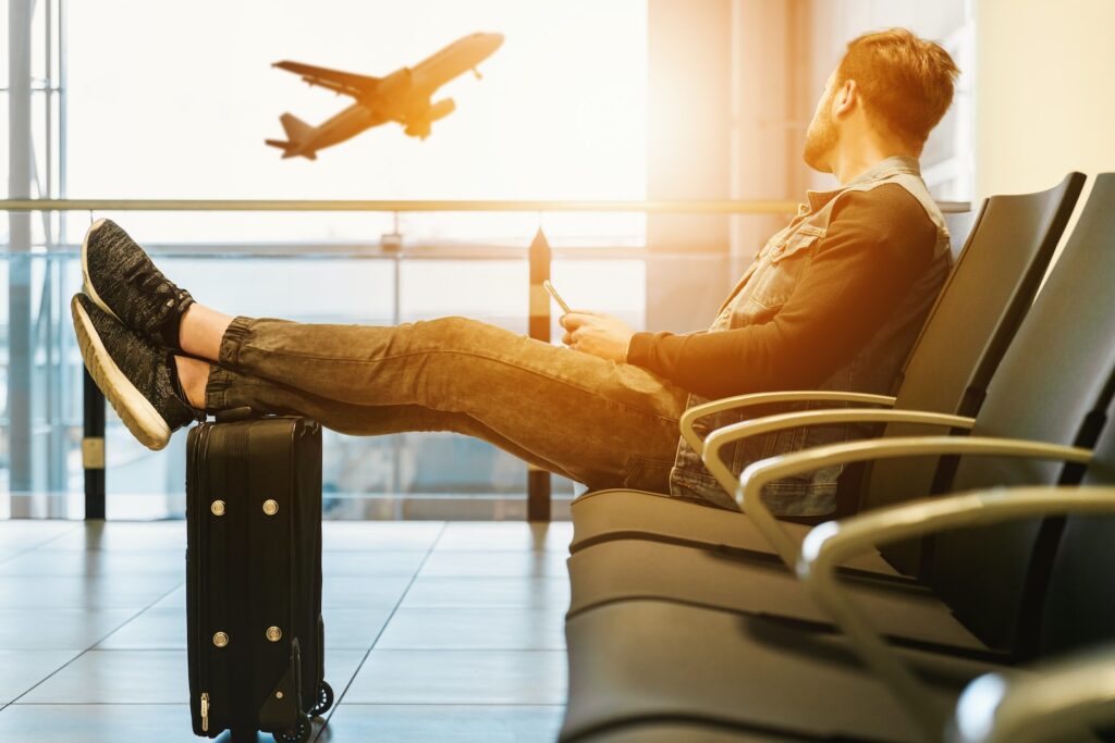 Travel Insurance - man sitting on gang chair with feet on luggage looking at airplane